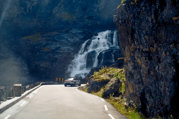 A high-end modern car driving through a sunlit mountain pass representing freedom and security